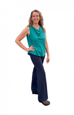Kari wearing blue trousers and a teal sleeveless top, standing and smiling